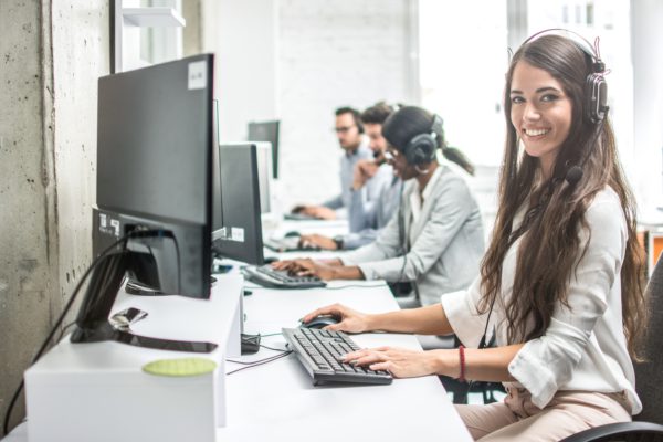 Beautiful smiling woman costumer support worker with headset using computer in call center.